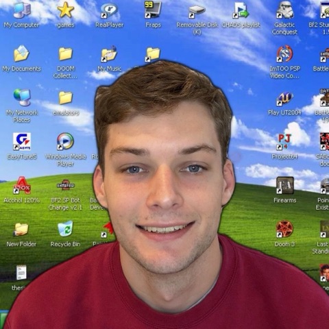 Yates smiling in front of a Windows XP desktop wallpaper covered in game icons